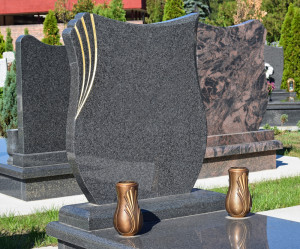 New granite headstone, shaped like a shield with gold engraving, in cemetery